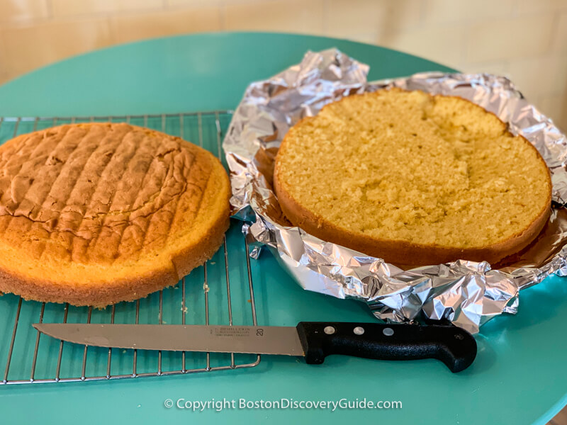 Sponge cake sliced in half horizontally, with bottom layer on cake plate protected by aluminum foil strips