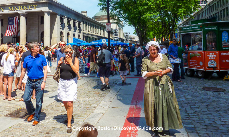 Tour guide in Colonial costume standing next to the Freedom Trail's red stripe at Faneuil Marketplace