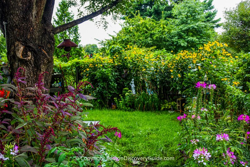 This pastoral garden focuses on a grassy lawn, beautiful flowers, bird feeders, and the small statue in the back